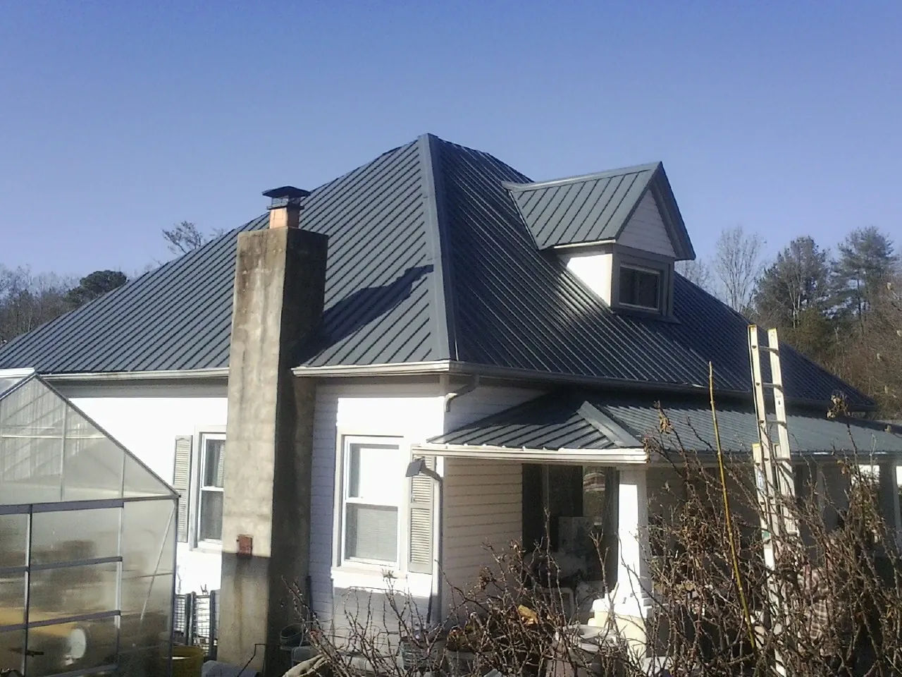 Dark blue standing seam metal roof on a white farmhouse with dormer — Slate & Tile Roof Repair by Roofing Brothers in Rives