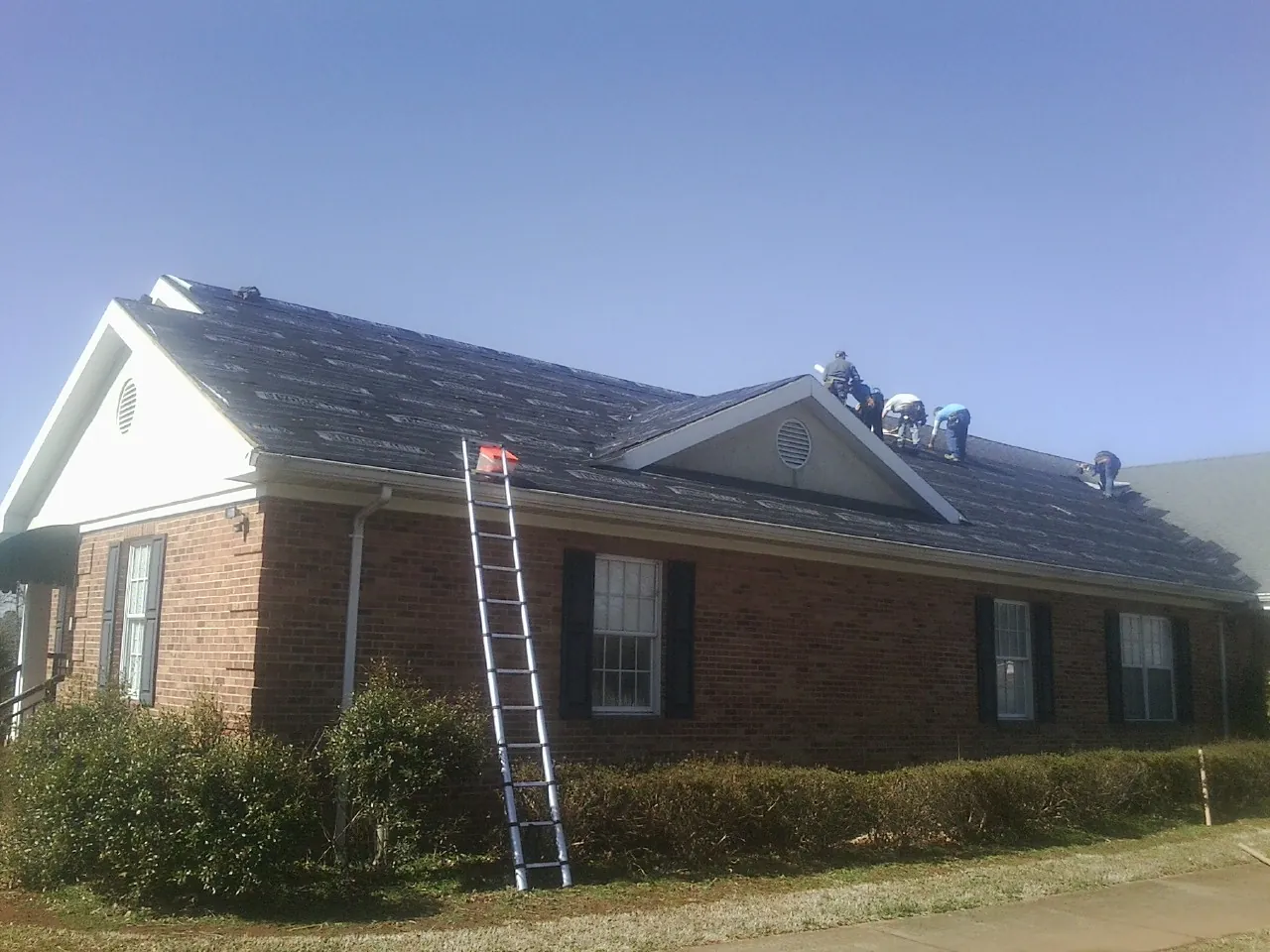 Crew tearing shingles off a brick ranch roof with a ladder set — Metal Roof Repair work by our crew in Rives