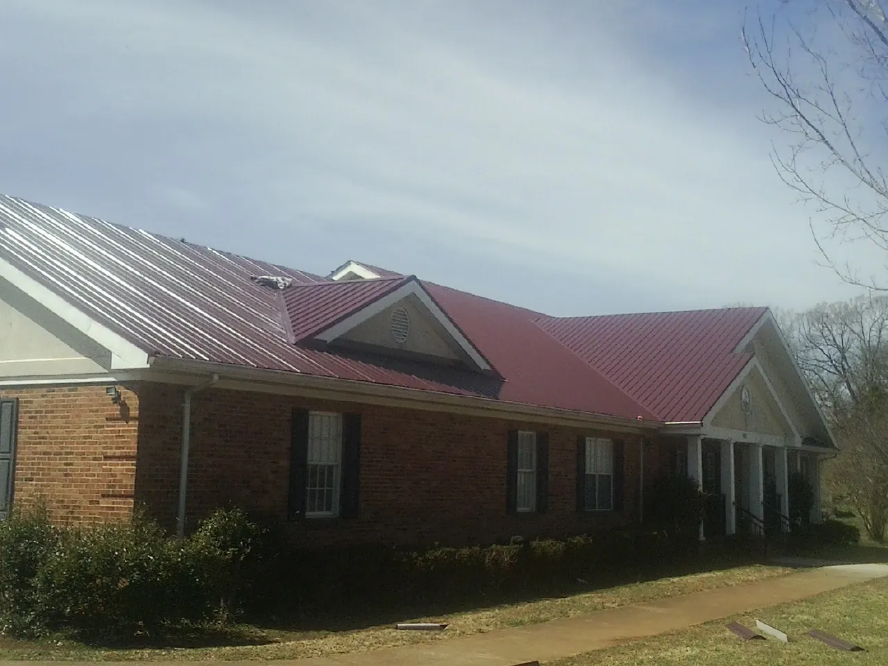 Red metal roof with gabled entries on a long brick building, from a Hail Damage Roof Repair job in Rives