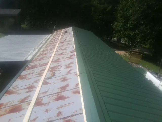 Old rusted panels beside newly installed green metal roofing — Wind Damage Roof Repair by Roofing Brothers in Rives