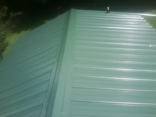 New green metal panels meeting at the ridge of a roof — Flat Roof Repair work by our crew in Rives