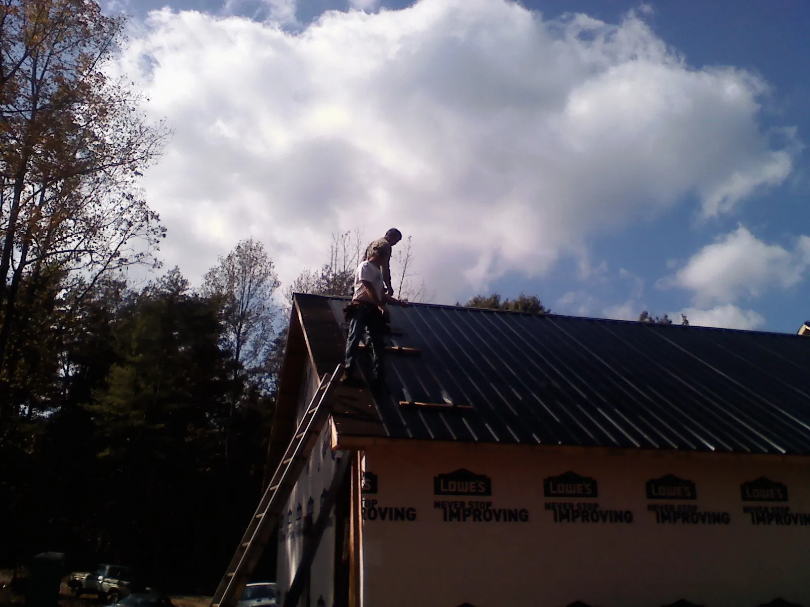 Roofer fastening dark metal panels high against a cloudy sky, from a Roof Inspection job in Rives