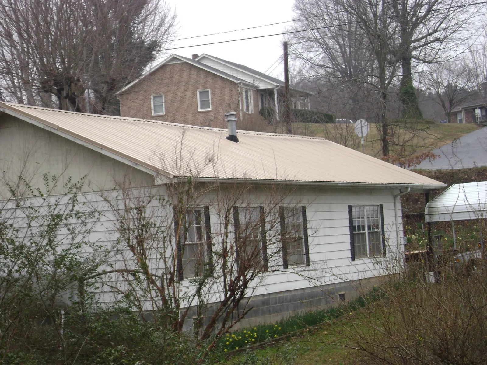 Tan metal roof on a white sided house set into a hillside — Commercial Roofing by Roofing Brothers in Rives
