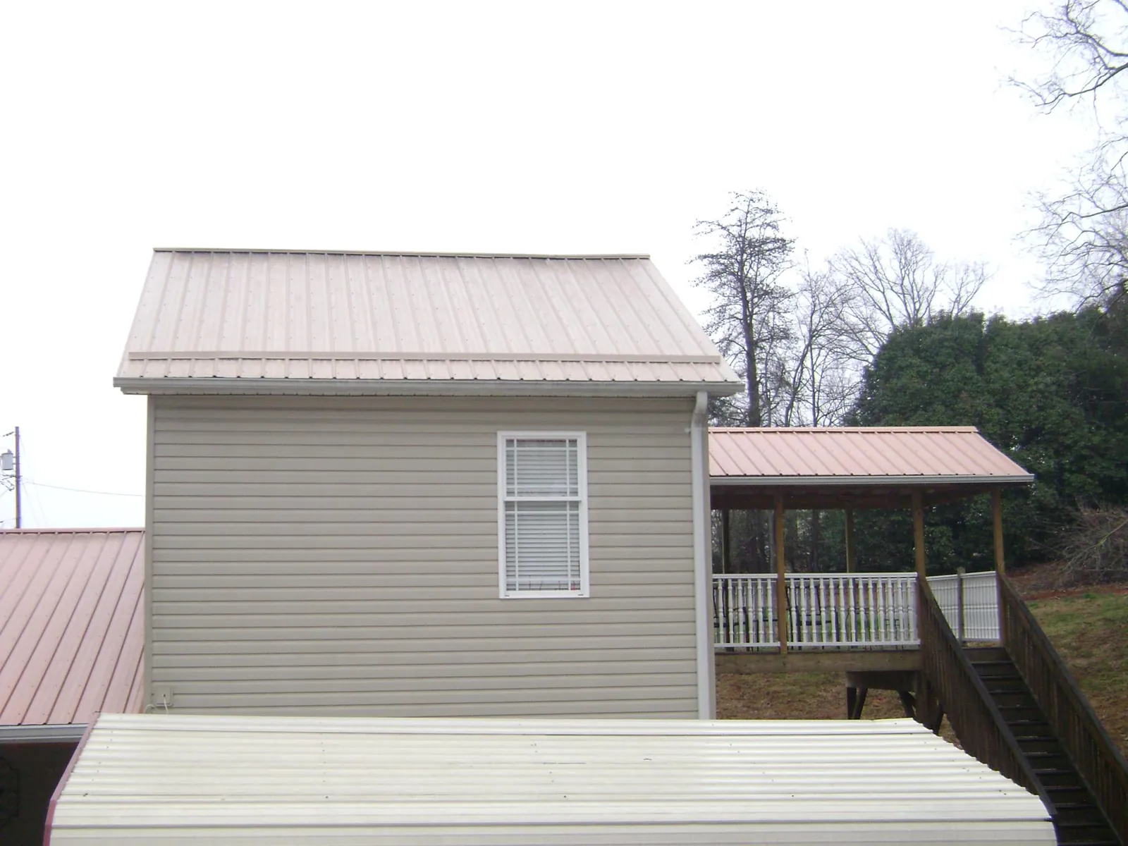 Tan metal roofs on a two story addition and attached porch, from a Roof Replacement job in Rives
